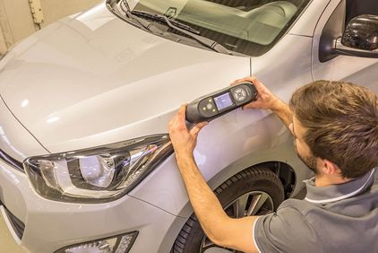 Mann kontrolliert Lackierung mit Messgerät