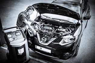Mann steht bei offener Motorhaube und begutachtet die Technik