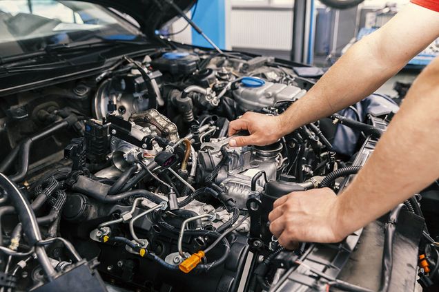 Arme eines Technikers bearbeiten den Motor in der offene Motorhaube eines PKWs.